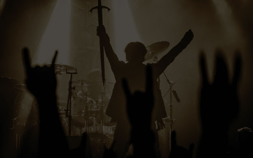 cantante de armored dawn, banda brasileña, sosteniendo una espada hacia abajo durante un concierto en vivo. a contraluz, se observan las manos del público haciendo la seña de cuernos.